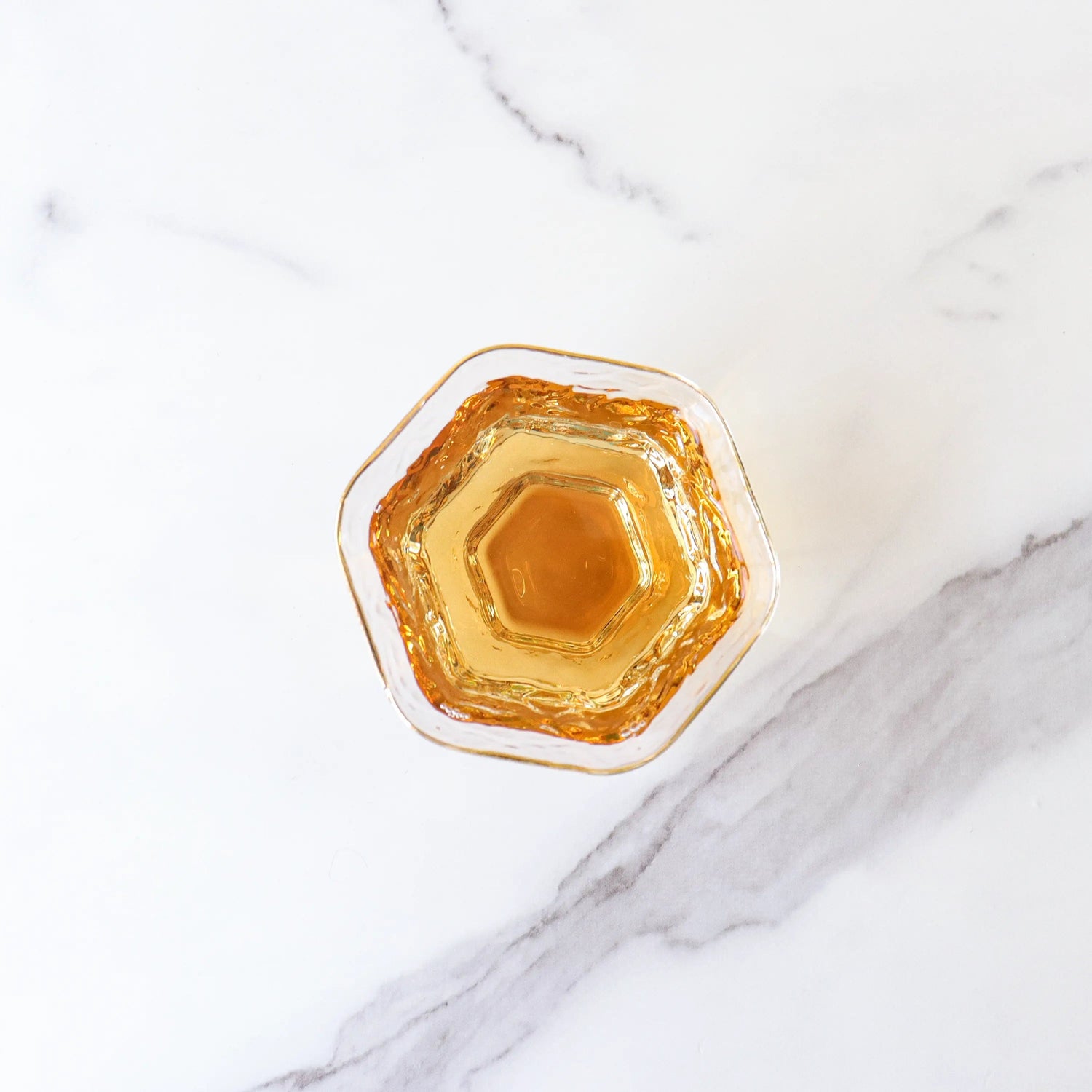 A hexagonal glass filled with My Store’s Dianhong Rose Black Tea sits on a white marble surface, its amber hue reminiscent of Yunnan rose petals.