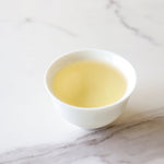 A white cup filled with light yellow Biluochun Green Tea from My Store, known for its rich antioxidants, rests on a white marble surface.
