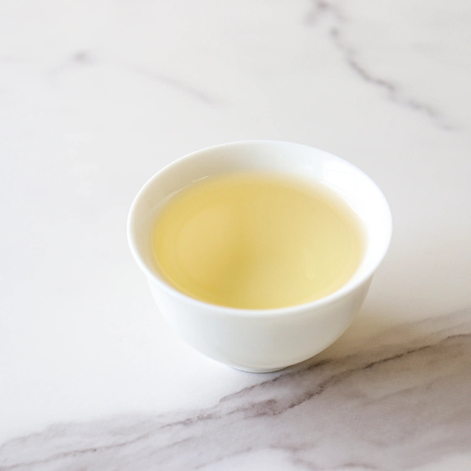 A white cup filled with light yellow Biluochun Green Tea from My Store, known for its rich antioxidants, rests on a white marble surface.
