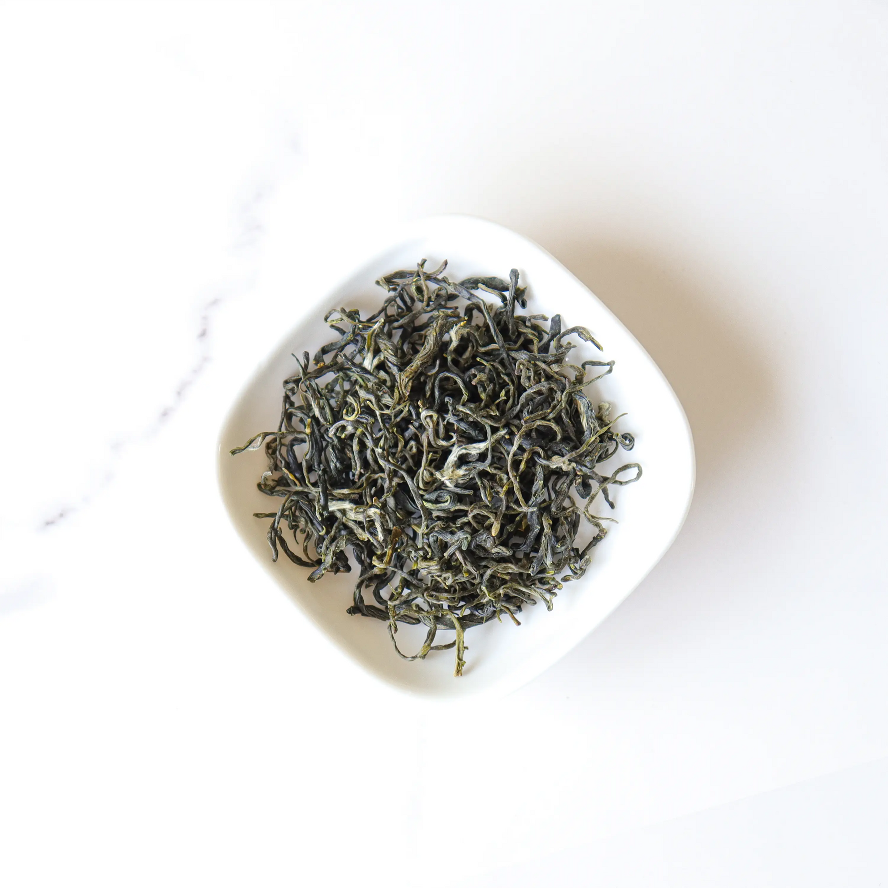 A white bowl of My Store Biluochun Green Tea loose leaves sits on a white surface, highlighting its rich antioxidants.