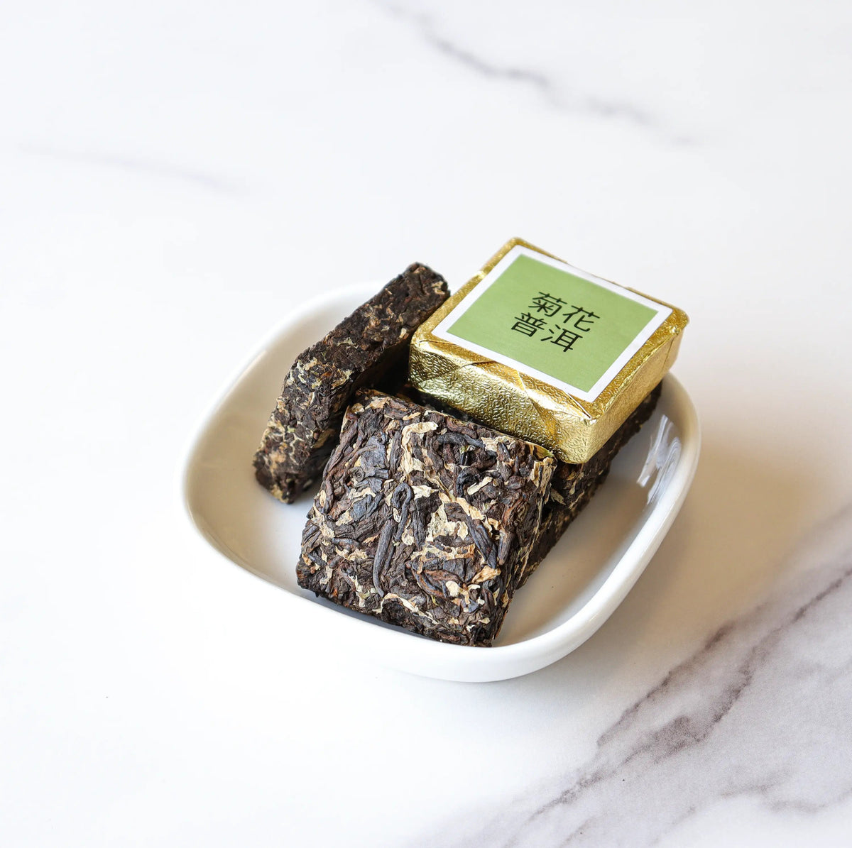CHICHATEA Mini Chrysanthemum Pu-erh Tea Cakes in a white dish with gold wrapper