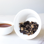 A white bowl with Small Chrysanthemum Pu‘er Tea Cakes by My Store sits beside a cup of brewed tea on a white surface.
