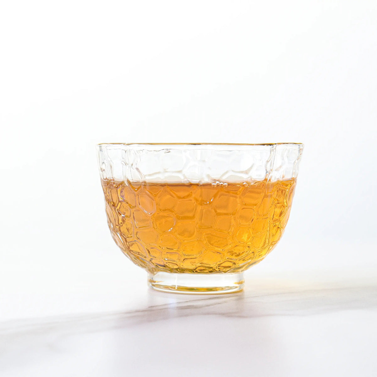 Brewed Da Hong Pao Oolong Tea liquor in a clear glass cup on a white surface.
