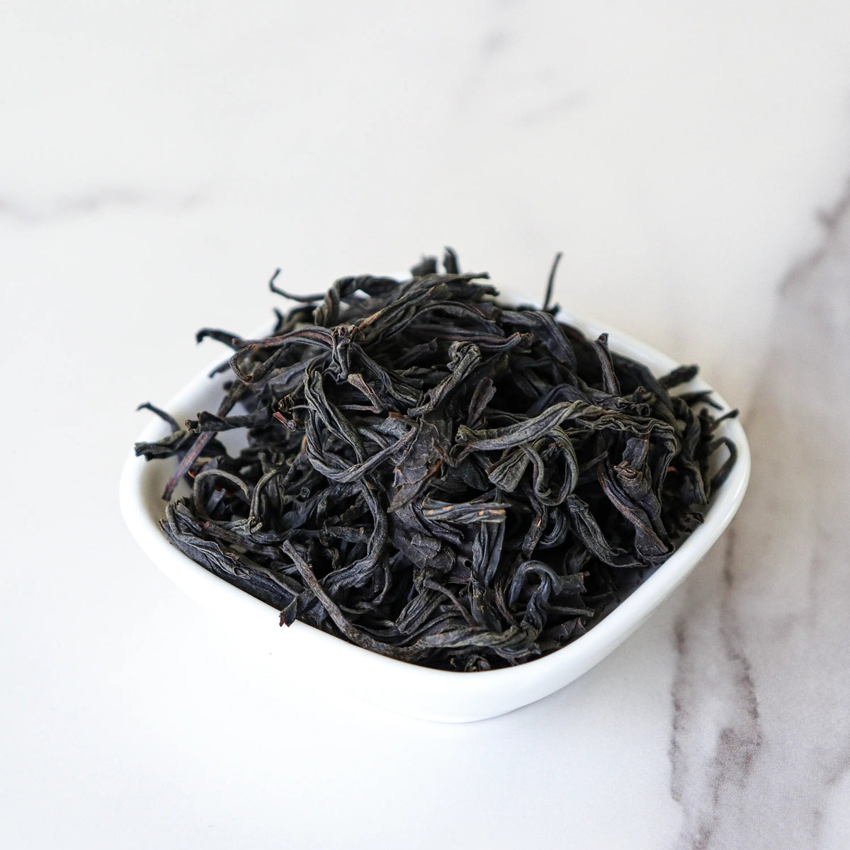 Loose Da Hong Pao Oolong Tea leaves in a white bowl on a marble surface.
