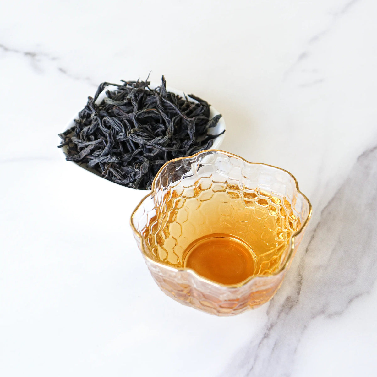 Da Hong Pao Oolong Tea dry leaves beside amber tea liquor in a glass cup.