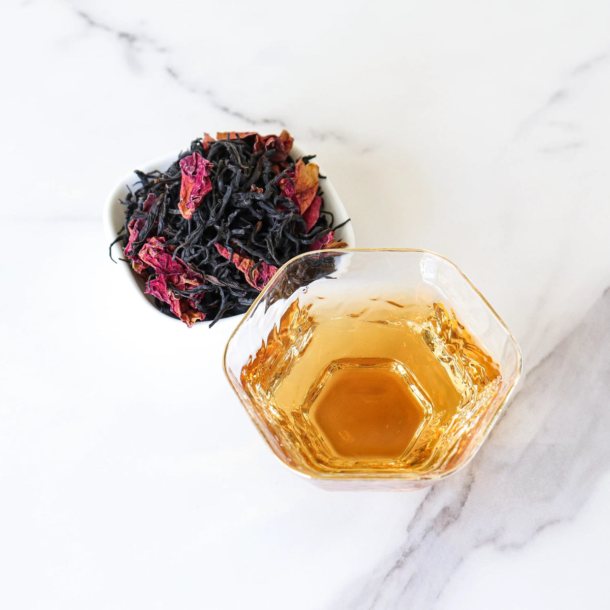 CHICHATEA Dianhong Rose Black Tea in a glass cup beside loose black tea leaves and dried rose petals