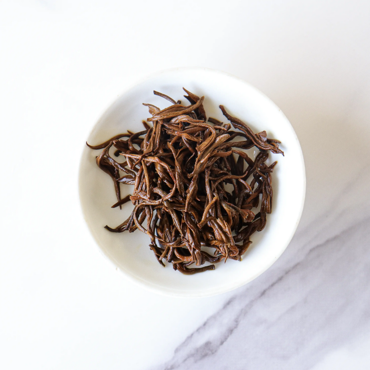 Loose Dianhong black tea leaves in a white bowl on a marble surface.