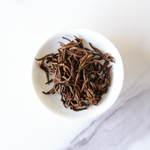 A white bowl filled with long, thin Dianhong Black Tea leaves from My Store sits on a white marble surface, highlighting this premium black tea.