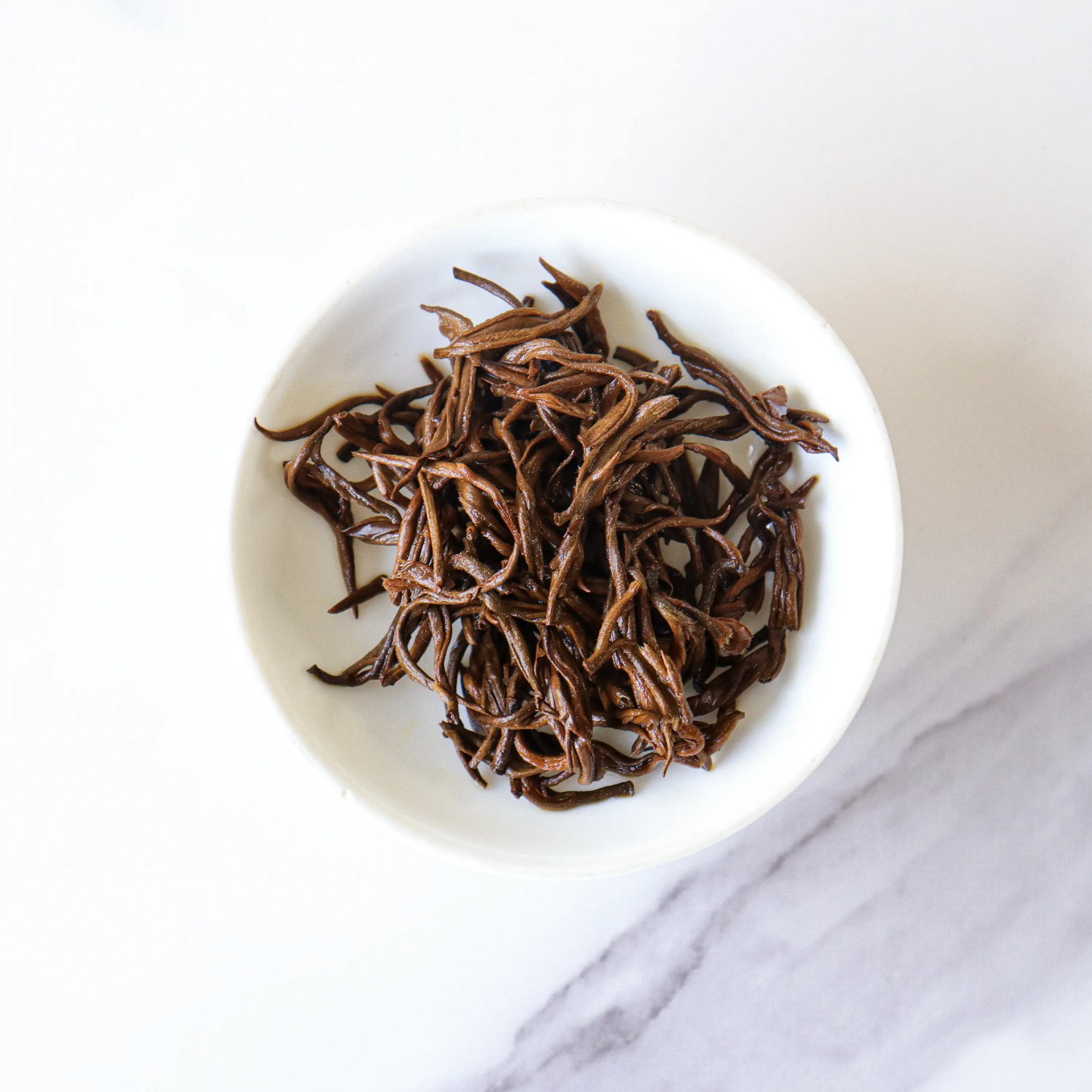 A white bowl filled with long, thin Dianhong Black Tea leaves from My Store sits on a white marble surface, highlighting this premium black tea.
