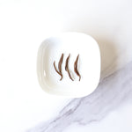 Three dried Dianhong Black Tea leaves from My Store are arranged side by side in a white square dish on a white and gray marbled surface, highlighting this premium black tea.