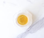 A white, textured bowl with pale yellow Dianhong Black Tea from My Store—renowned for its delicate, high-altitude flavor—rests on a white marble surface with gray veins.