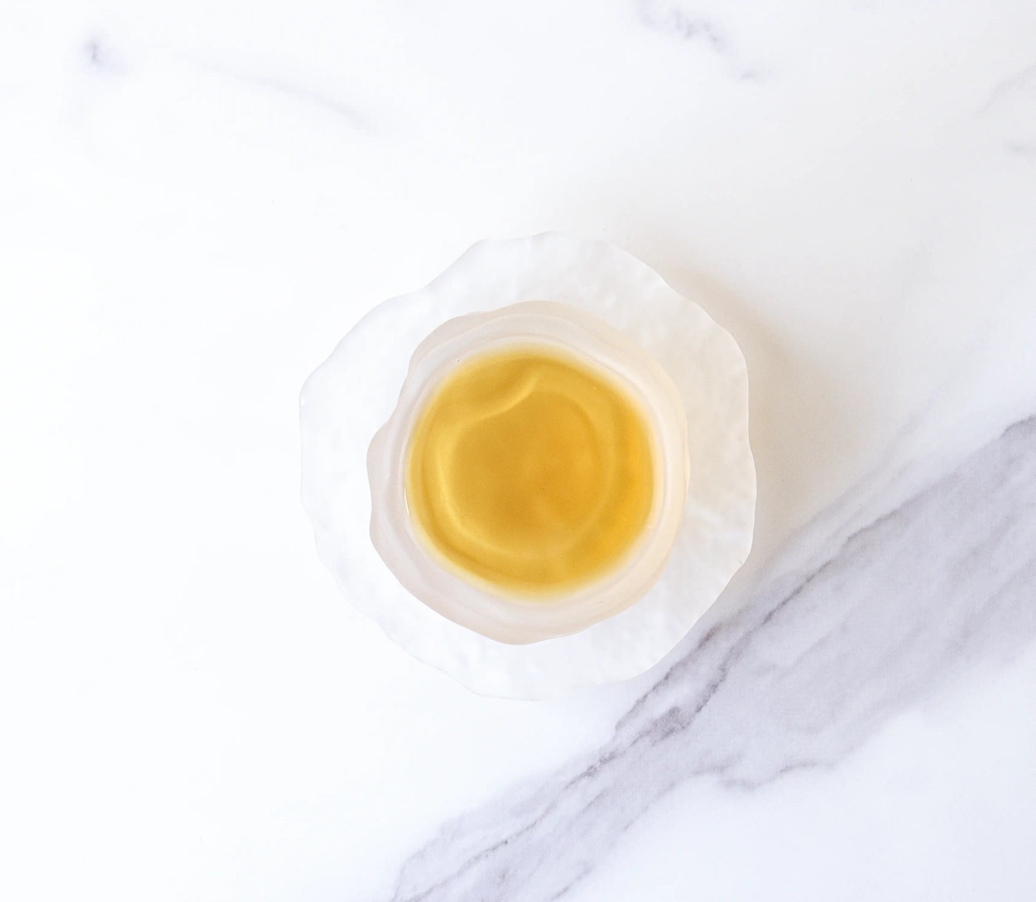 A white, textured bowl with pale yellow Dianhong Black Tea from My Store—renowned for its delicate, high-altitude flavor—rests on a white marble surface with gray veins.