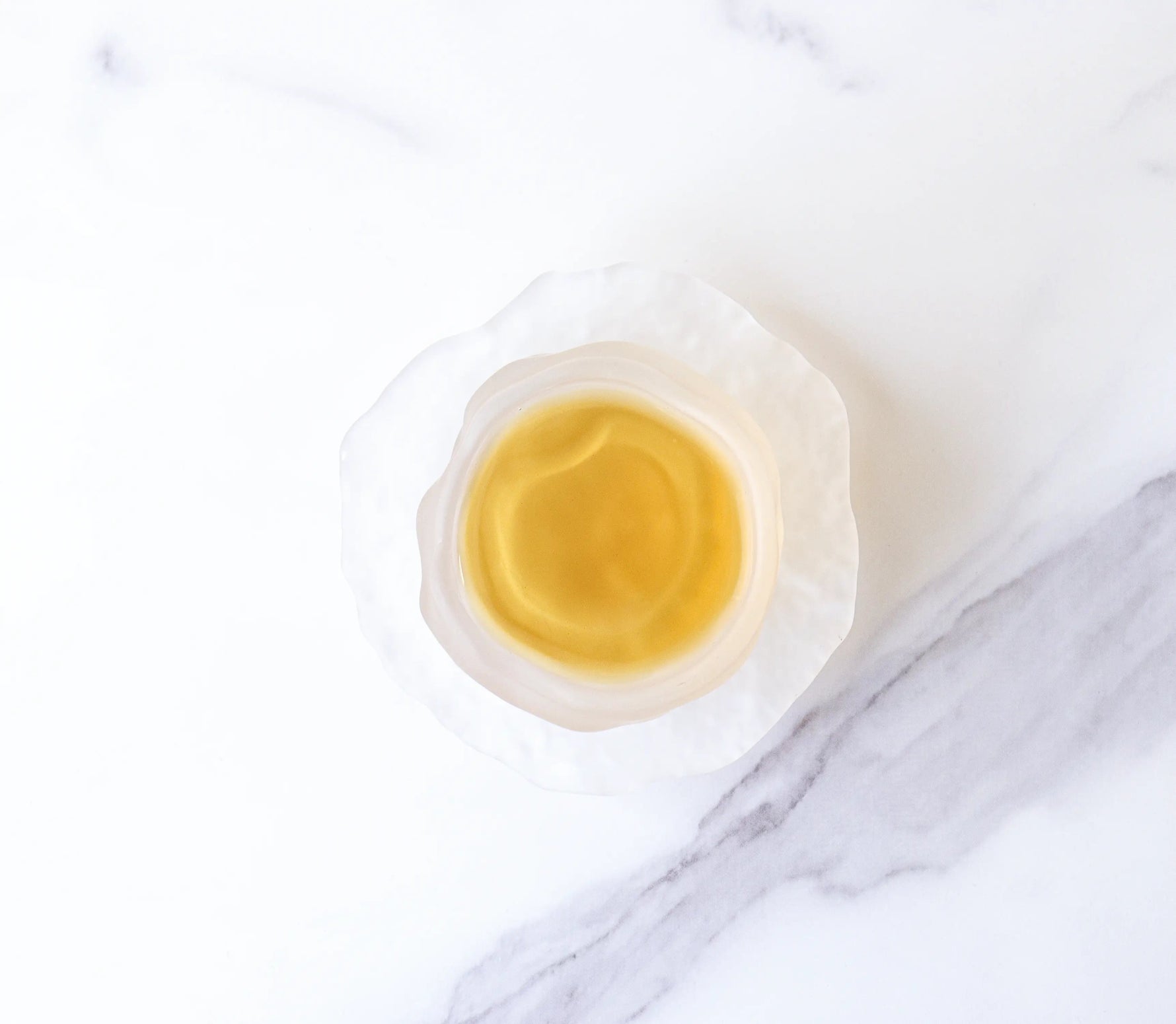 A white, textured bowl with pale yellow Dianhong Black Tea from My Store—renowned for its delicate, high-altitude flavor—rests on a white marble surface with gray veins.