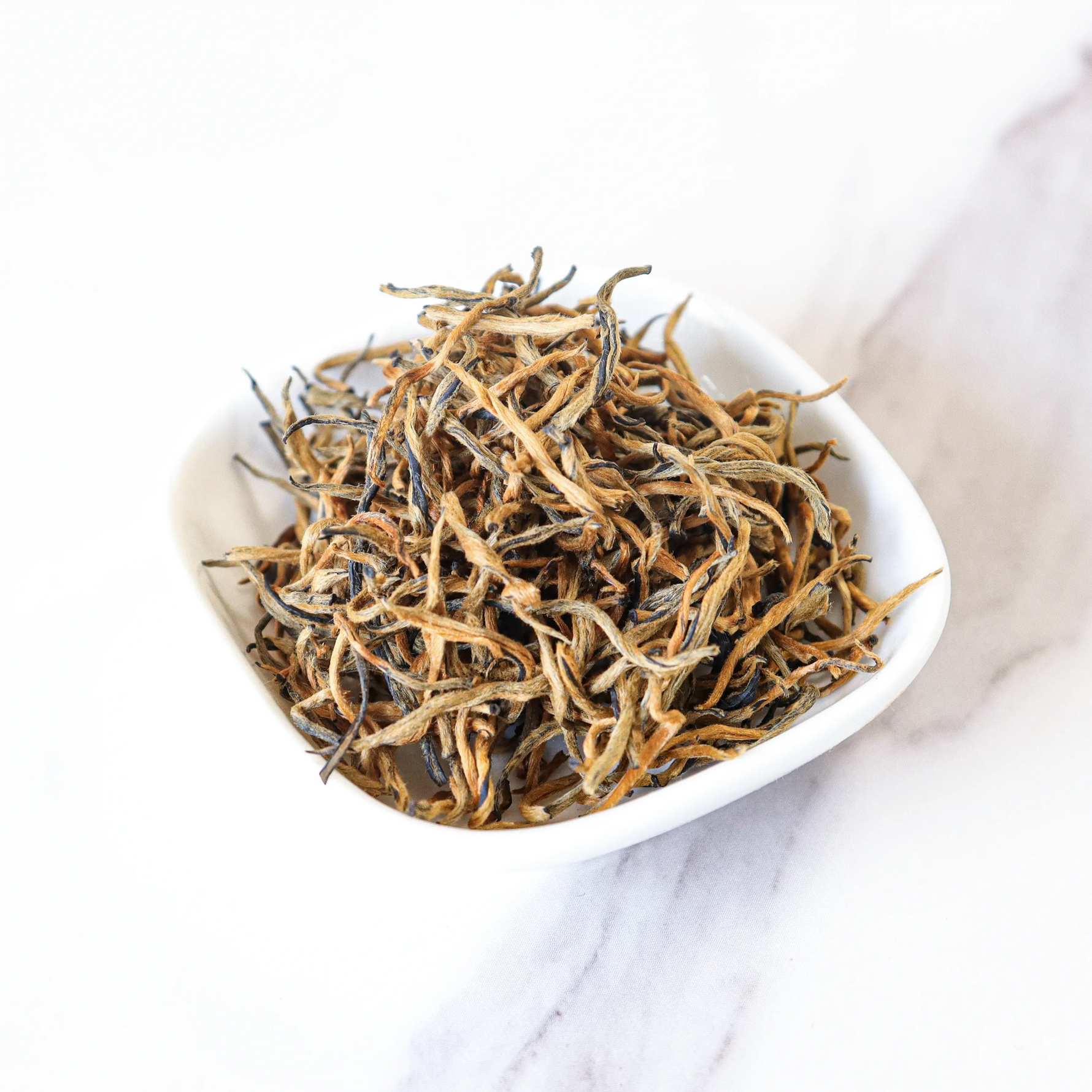 A small white dish holds loose Dianhong Black Tea leaves from My Store—premium black tea with golden and dark strands—displayed on a white marble surface.