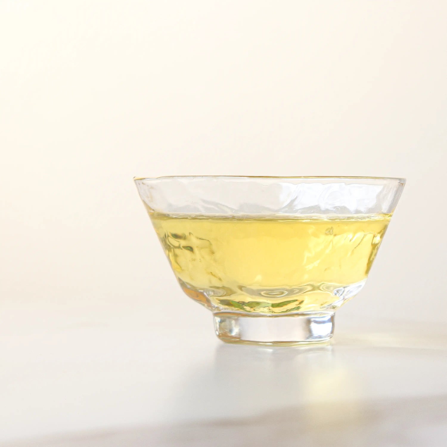 A clear glass cup holds light yellow Emei Maofeng Green Tea from My Store, resting on a light surface with a pale background.