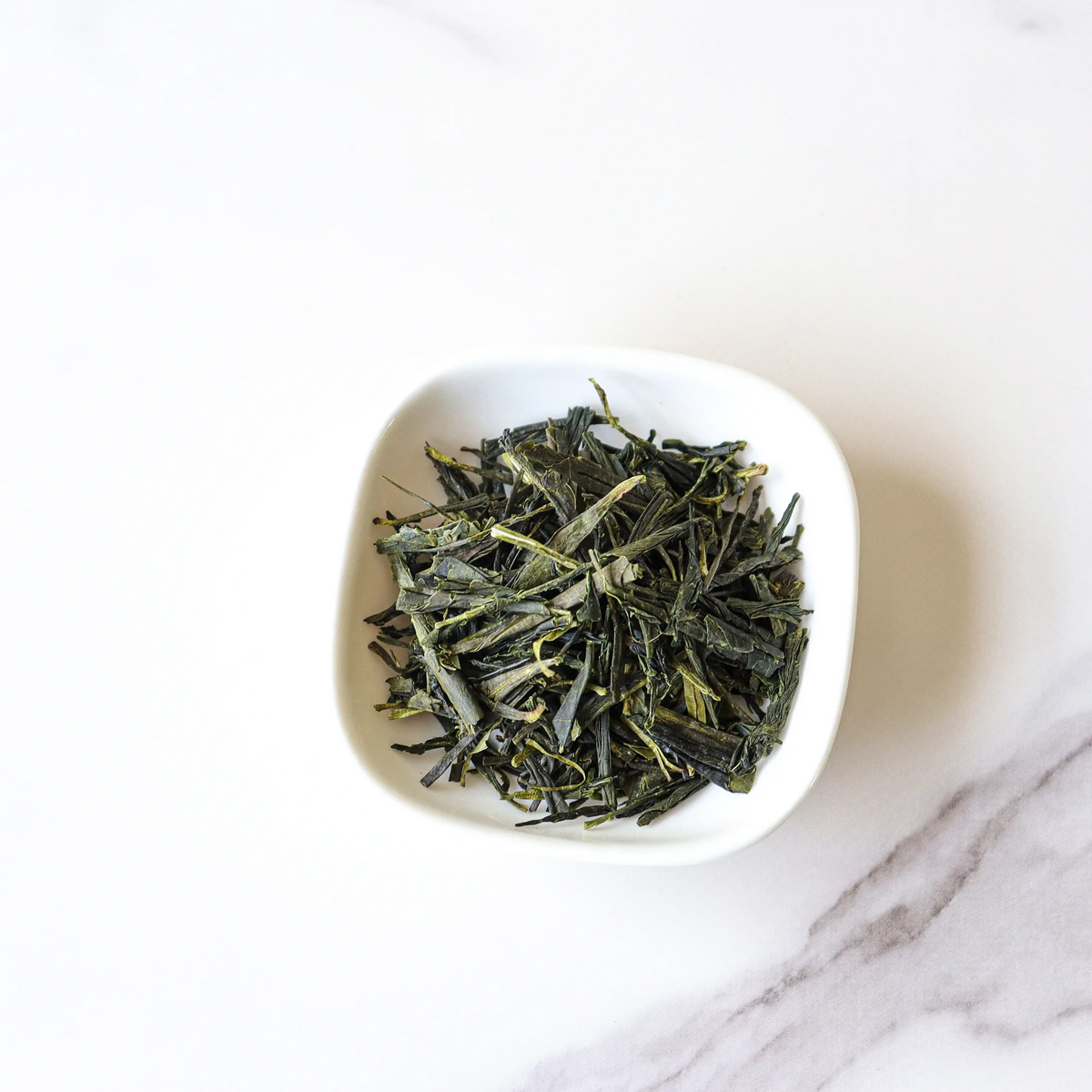 Enshi Yulu Green Tea loose leaves in a small white bowl on white marble