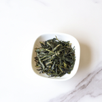 A small white bowl containing My Store's Enshi Yulu Green Tea, a premium loose-leaf Chinese green tea, sits on a white marble surface.