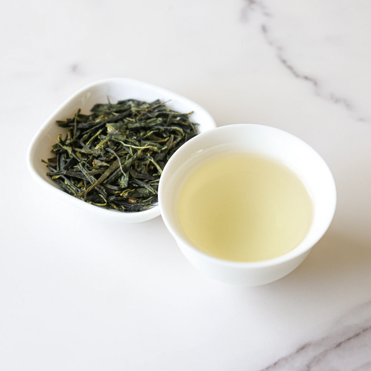 Enshi Yulu Green Tea loose leaves beside a cup of pale green tea