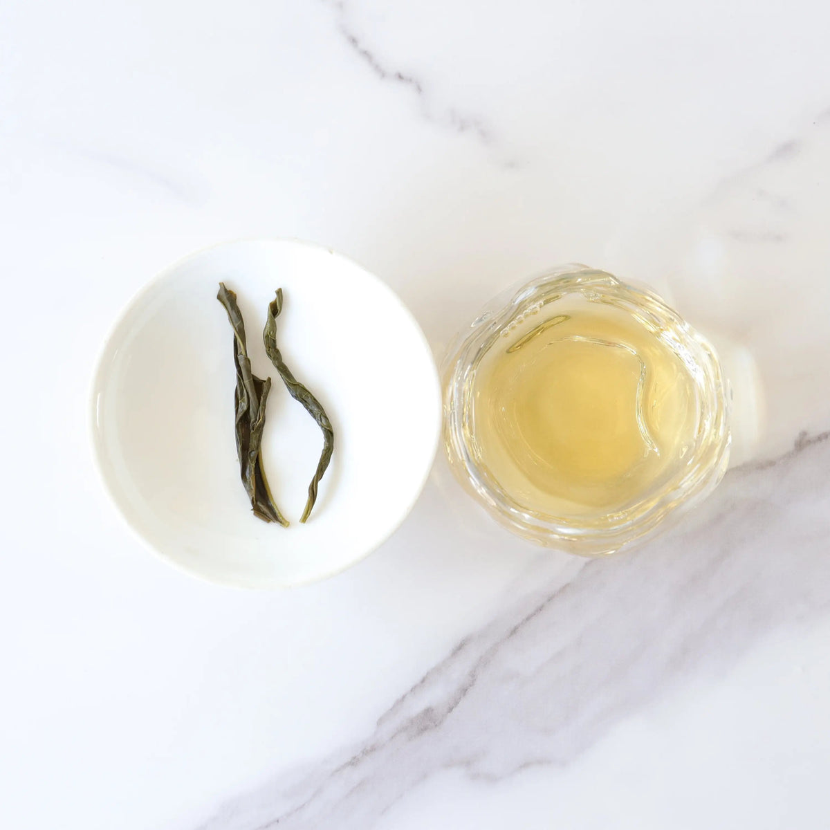 Gardenia Green Tea liquor beside steeped leaves on a small white dish