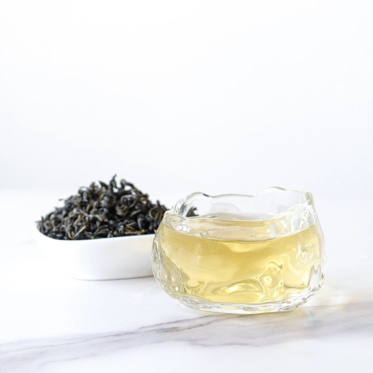 Gardenia Green Tea loose leaves beside brewed tea in a clear glass cup