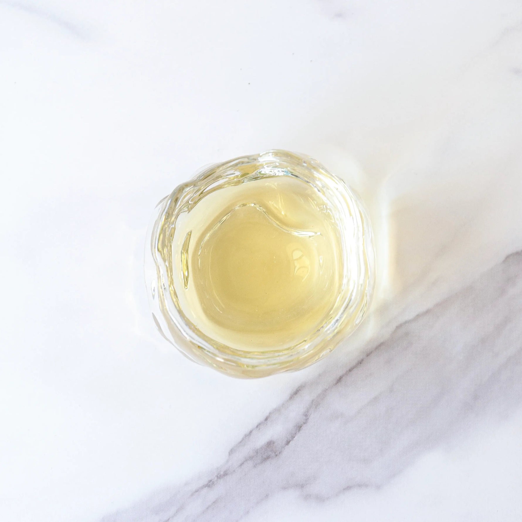 A small glass bowl filled with light yellow Gardenia Green Tea by My Store, placed on a white marble surface.