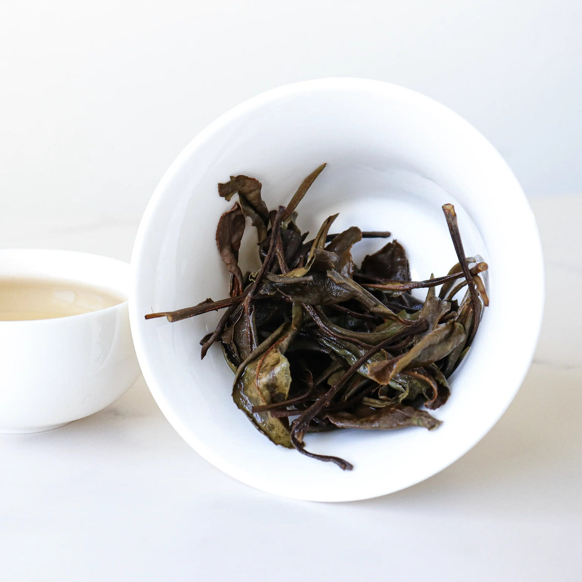 Steeped Gong Mei White Tea leaves beside a cup of brewed tea