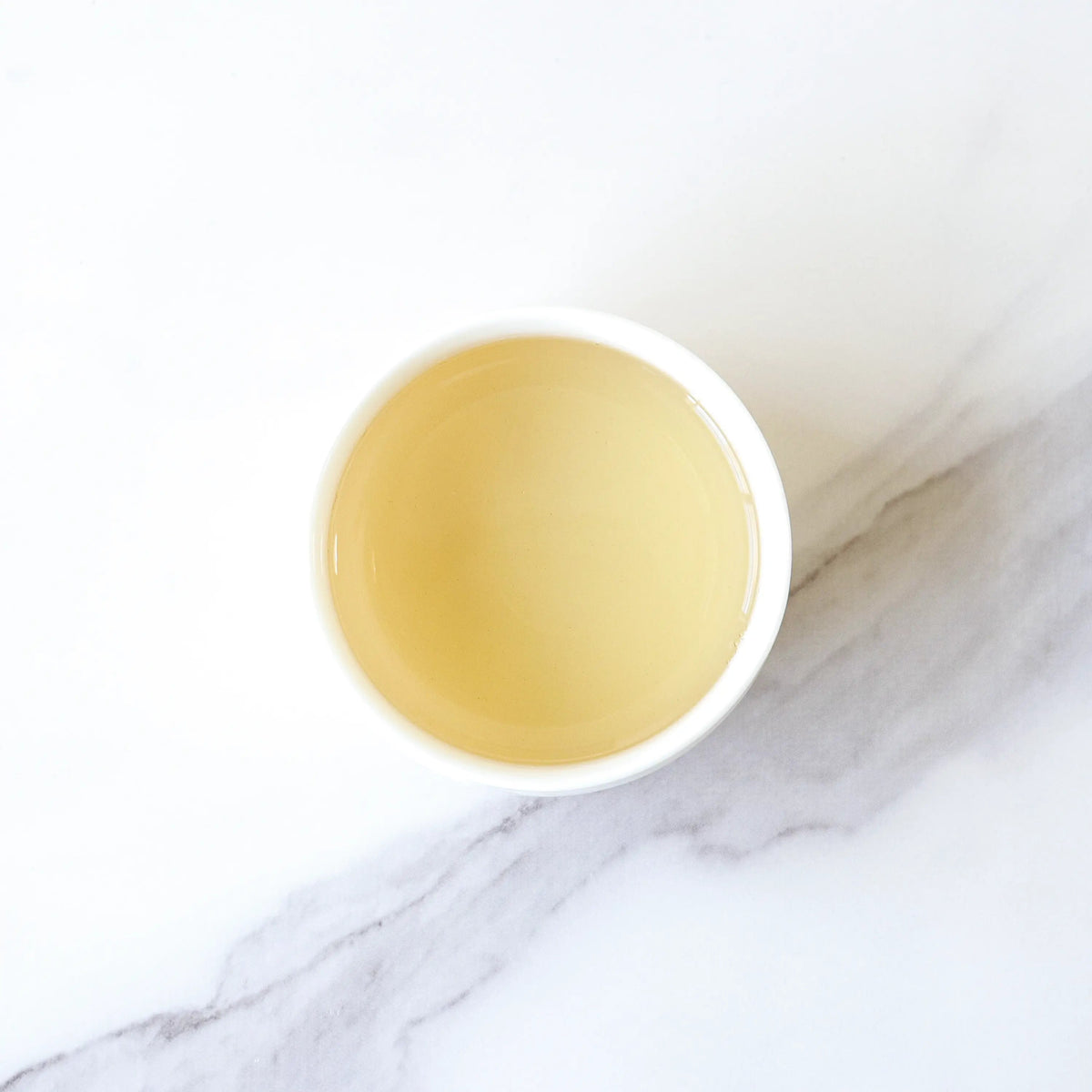 Light amber Gong Mei White Tea liquor in a white cup on marble
