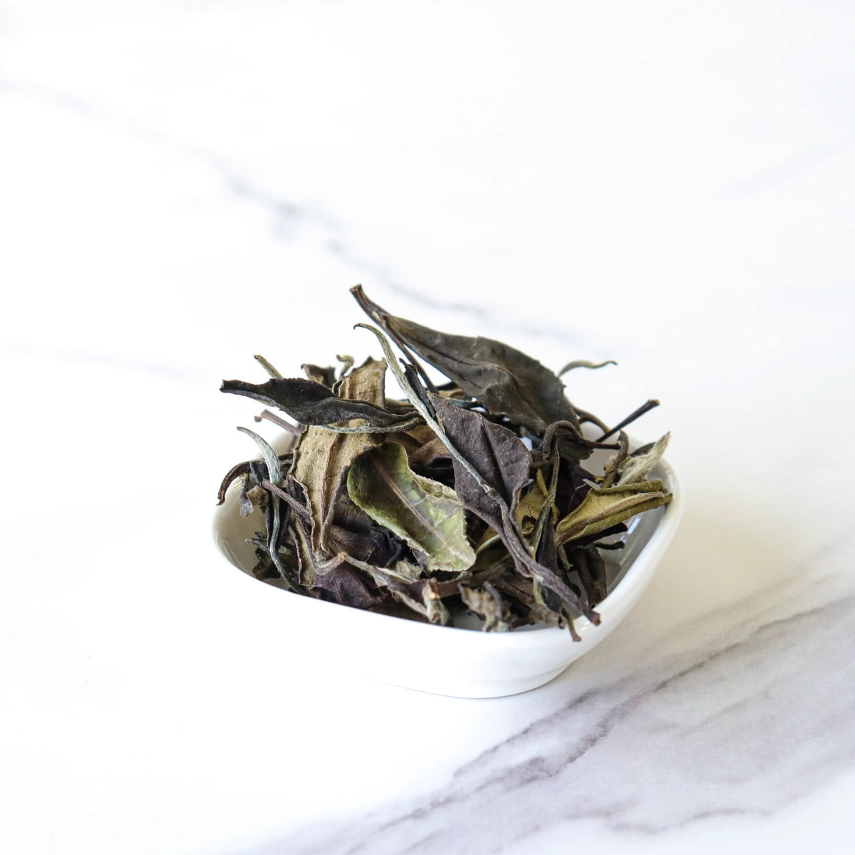 Gong Mei White Tea loose leaves in a small white bowl