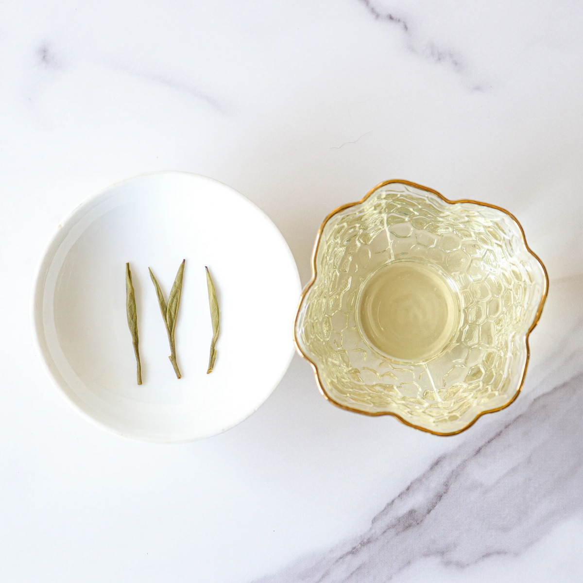Huangshan Maofeng Green Tea leaves on a white dish beside pale brewed tea.
