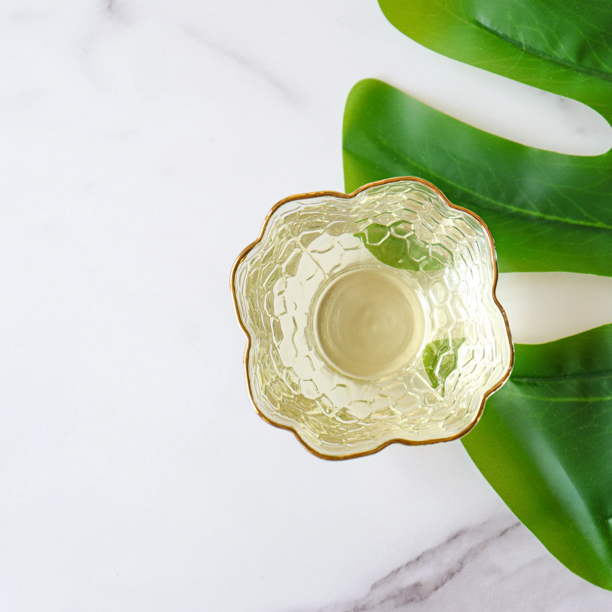 Brewed Huangshan Maofeng Green Tea in a glass bowl beside a green leaf.