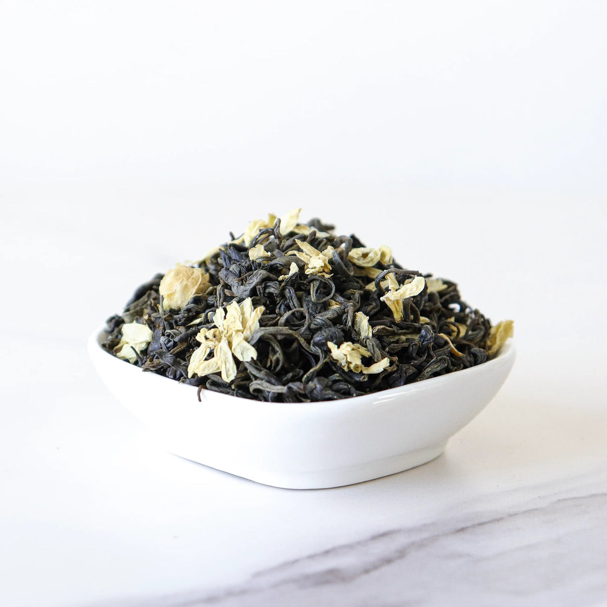 Loose leaf Jasmine Green Tea with jasmine petals in a white bowl.