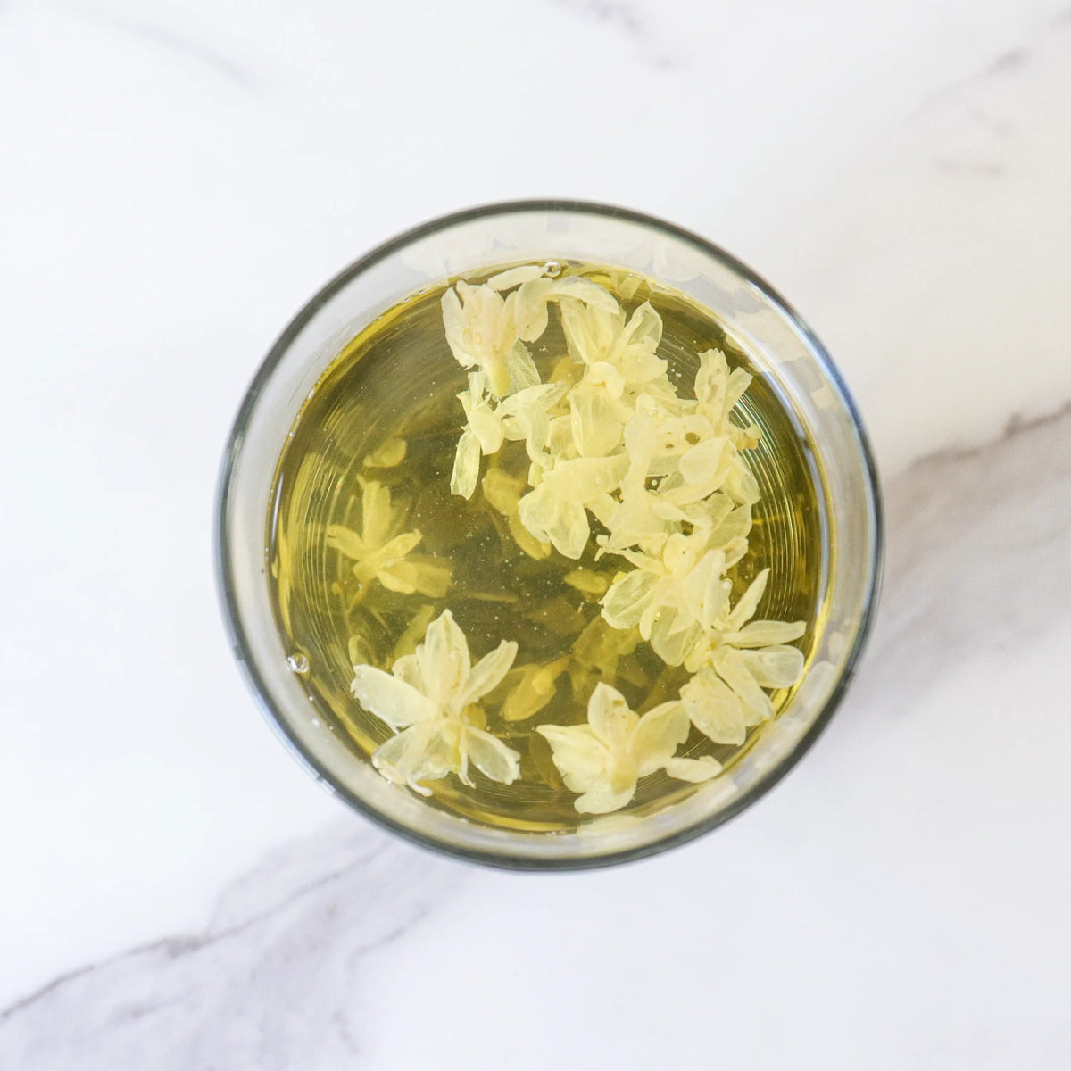 Top view of brewed Jasmine Green Tea with jasmine blossoms in a clear glass cup.