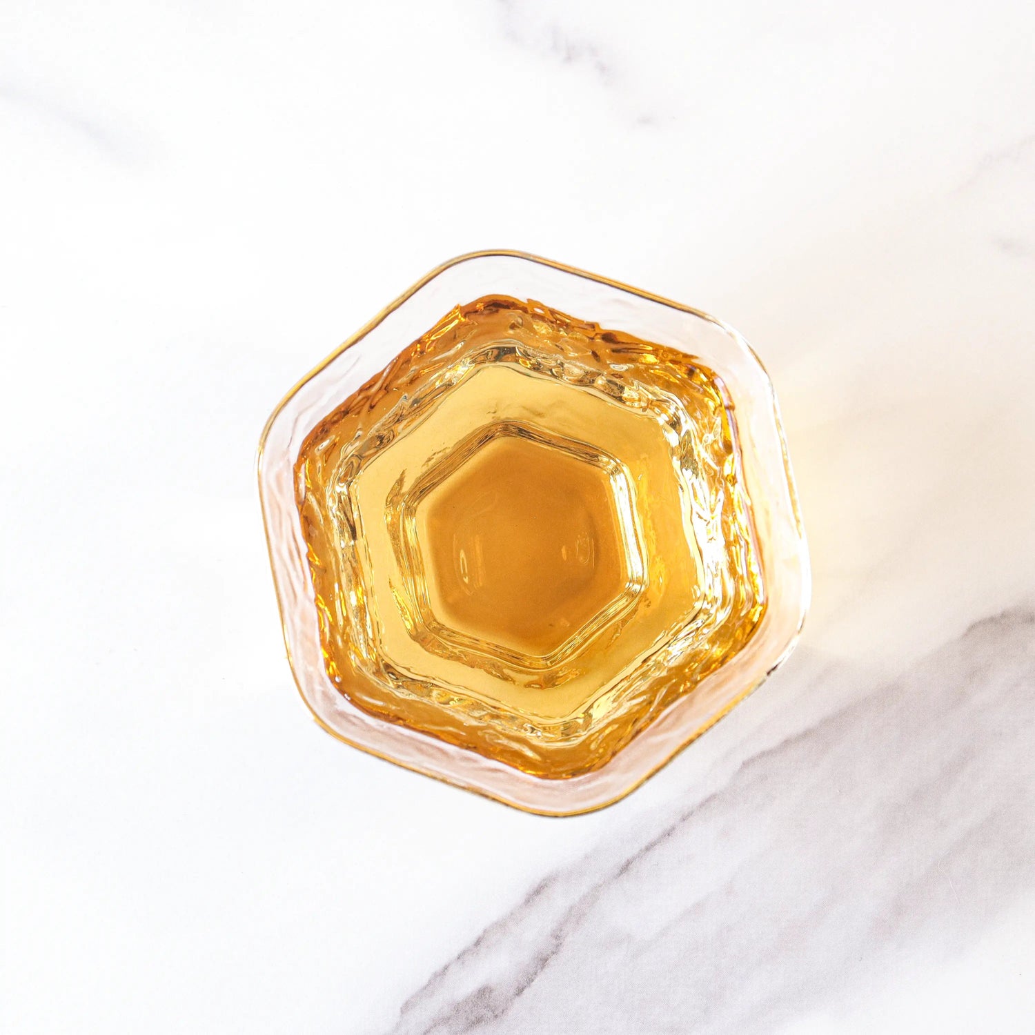 A hexagonal glass filled with golden-brown My Store Jin Jun Mei Black Tea loose leaves, seen from above on a white marble surface.