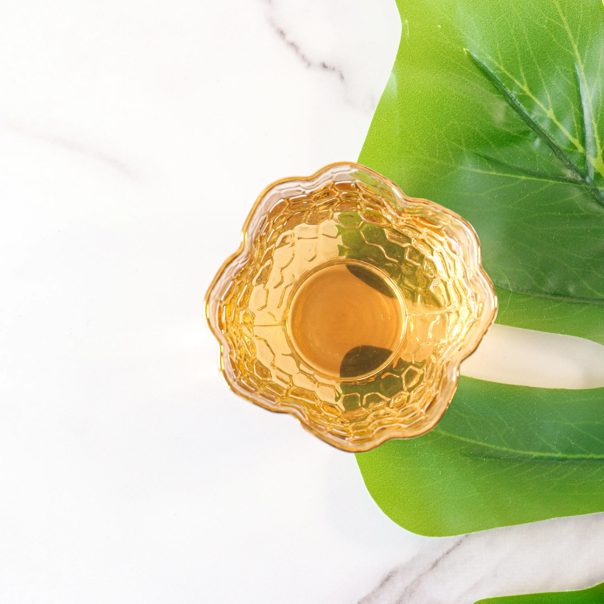 Brewed Keemun Black Tea in an amber glass bowl beside a green leaf.