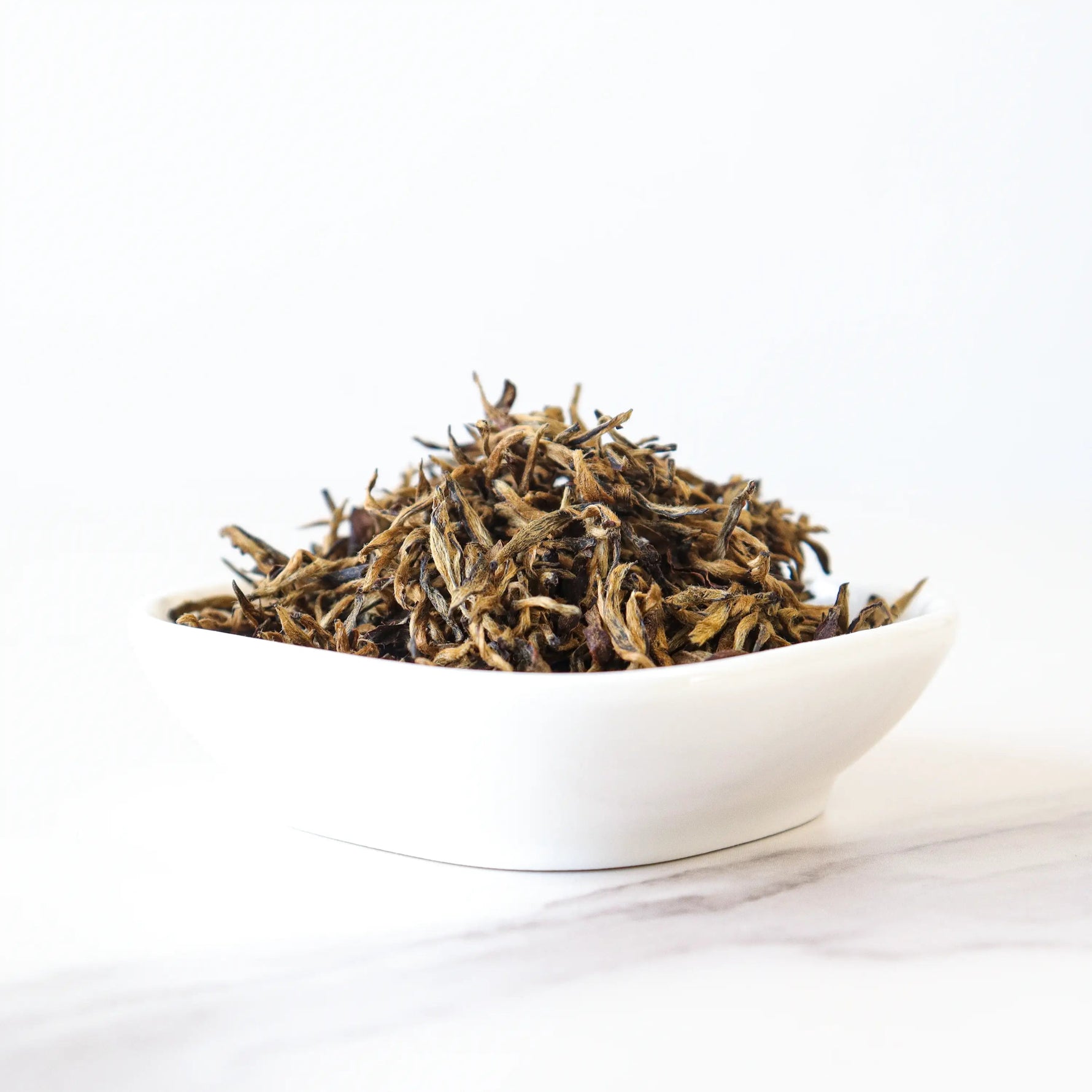 A white bowl filled with loose My Store Keemun Black Tea, the Queen of Black Tea, sits on a white marble surface against a plain white background.