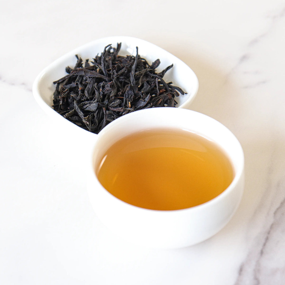 Brewed Lapsang Souchong Black Tea in a clear glass with loose tea leaves beside it.
