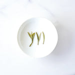 Three flat Longjing Dragon Well Green Tea leaves on a white tasting dish.