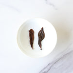 Two dried Oriental Beauty Oolong Tea leaves from My Store are placed side by side in a small white bowl on a white marble surface.