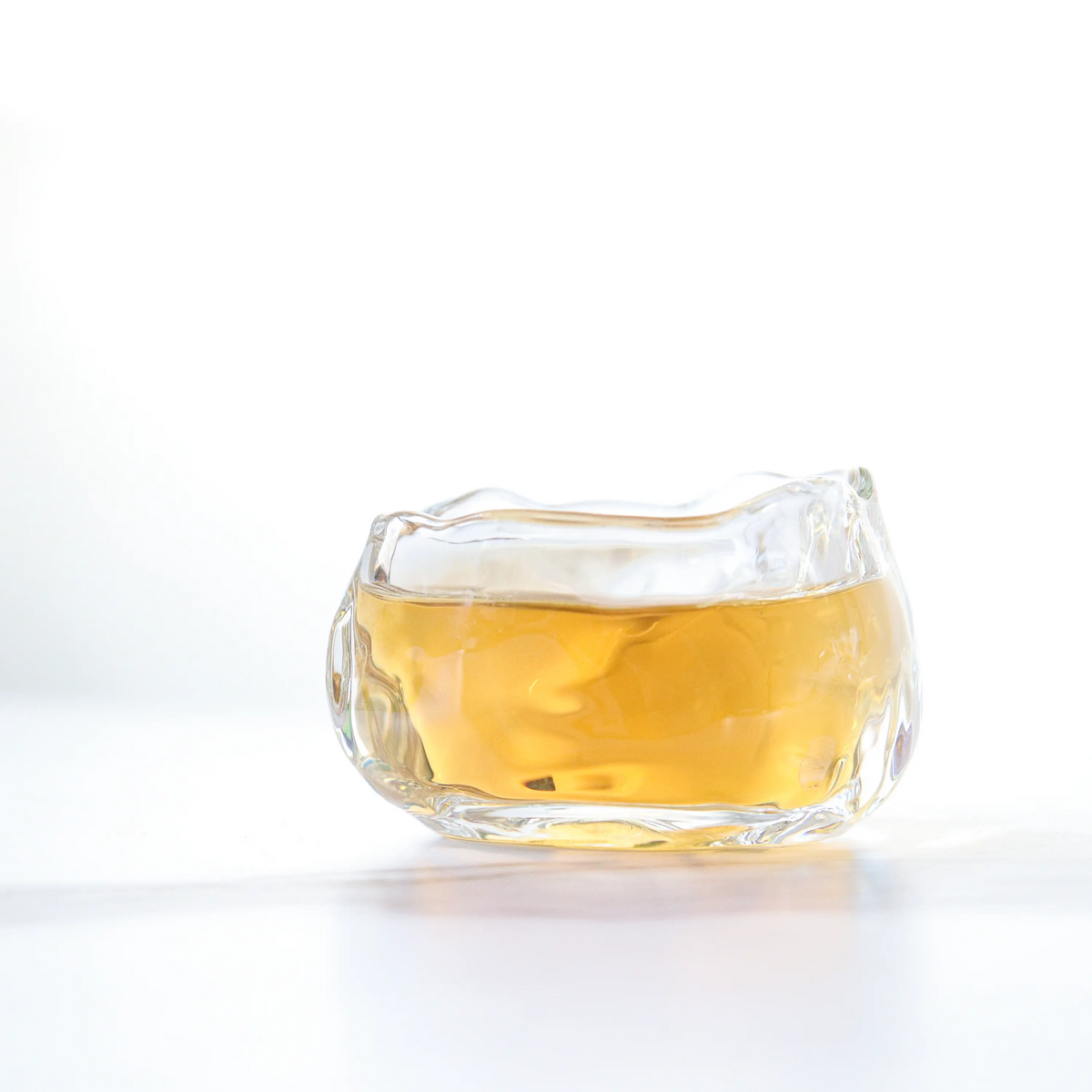 Brewed Oriental Beauty Oolong Tea in a small clear glass cup on a white surface.