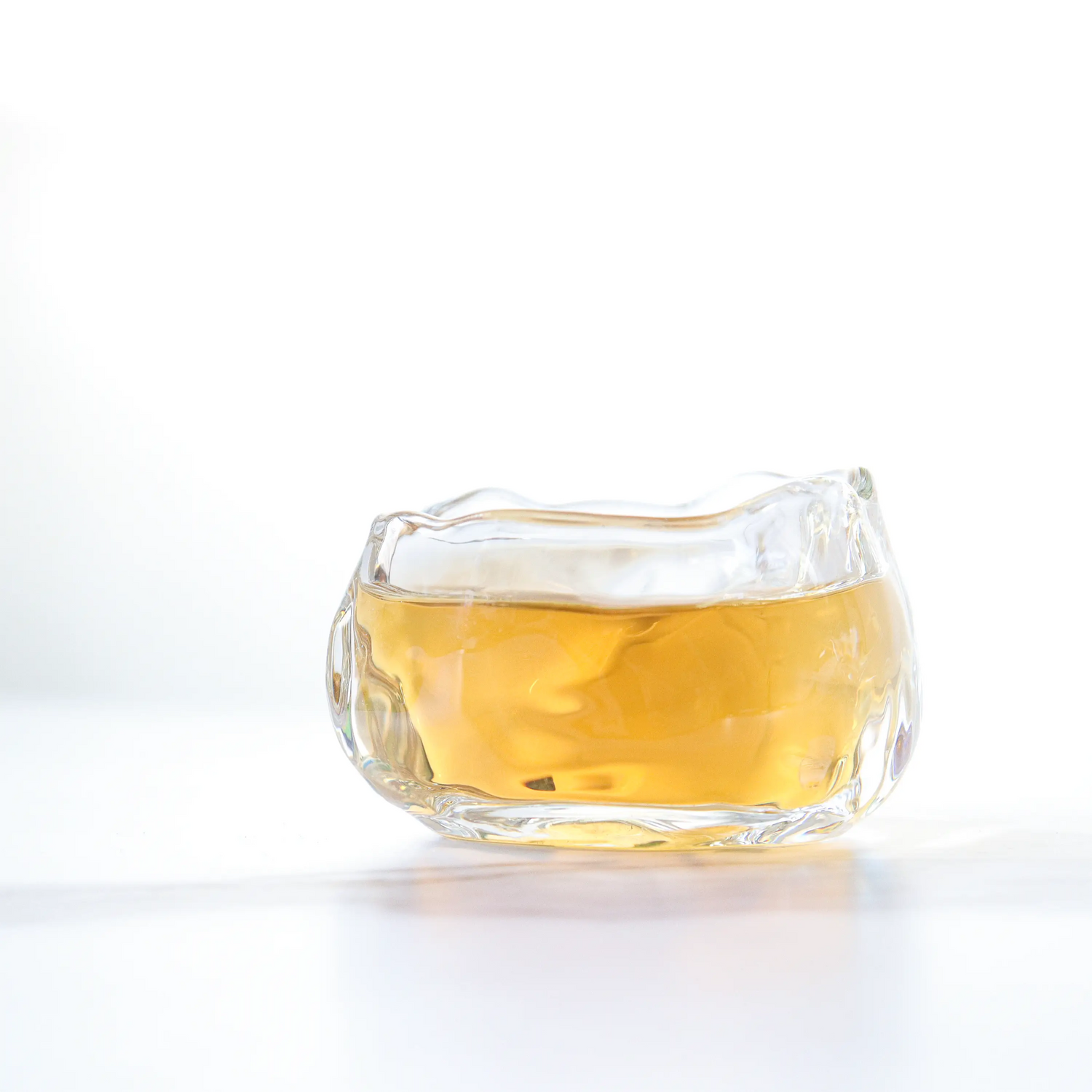 A clear glass cup with curved edges filled with light amber My Store Oriental Beauty Oolong Tea sits on a white surface against a white background.