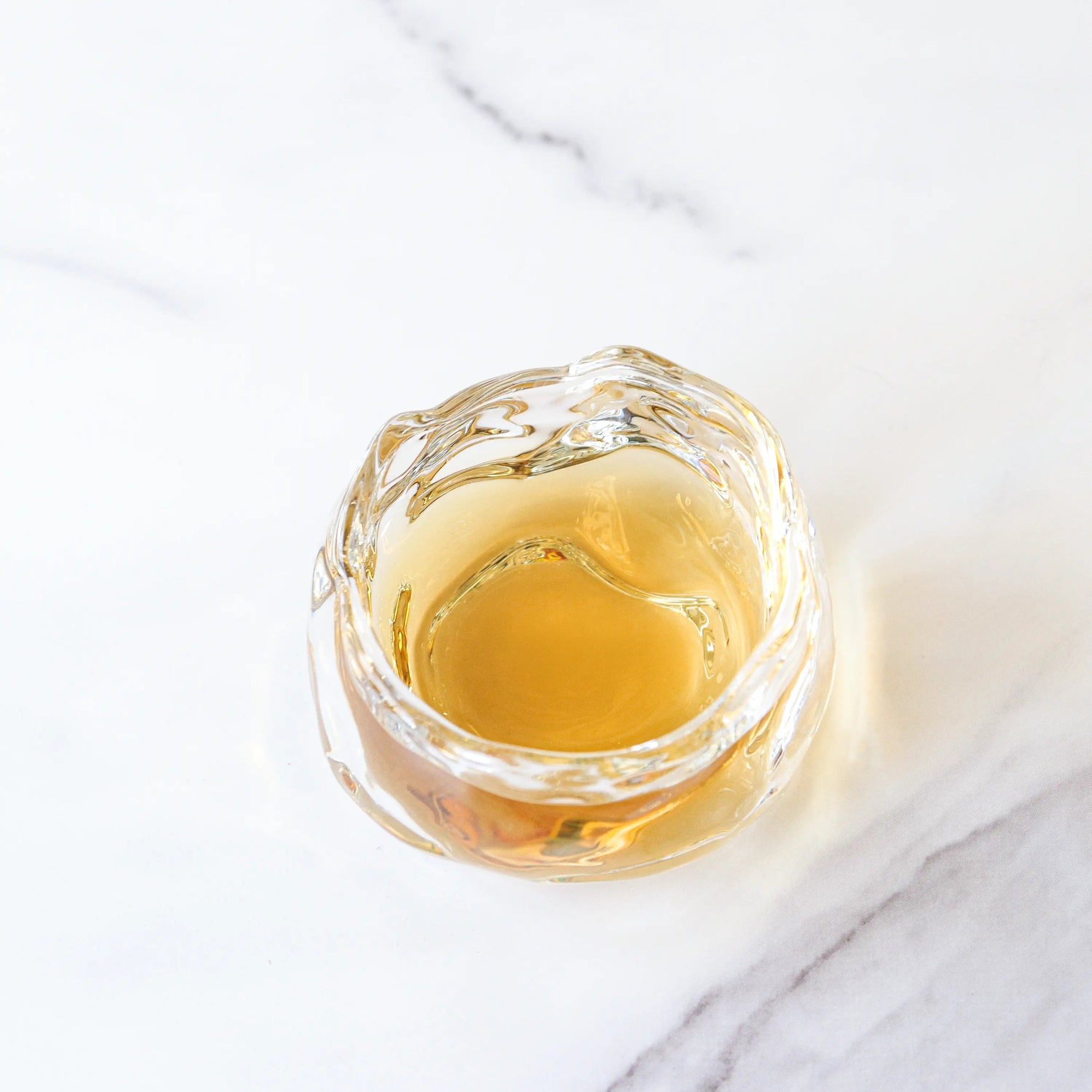 A small glass cup with light brown Oriental Beauty Oolong Tea from My Store sits on a white marble surface.