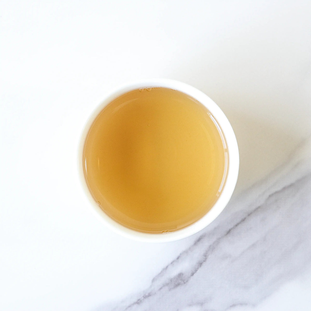Phoenix Dancong Oolong Tea golden tea liquor in a white cup on a marble surface.