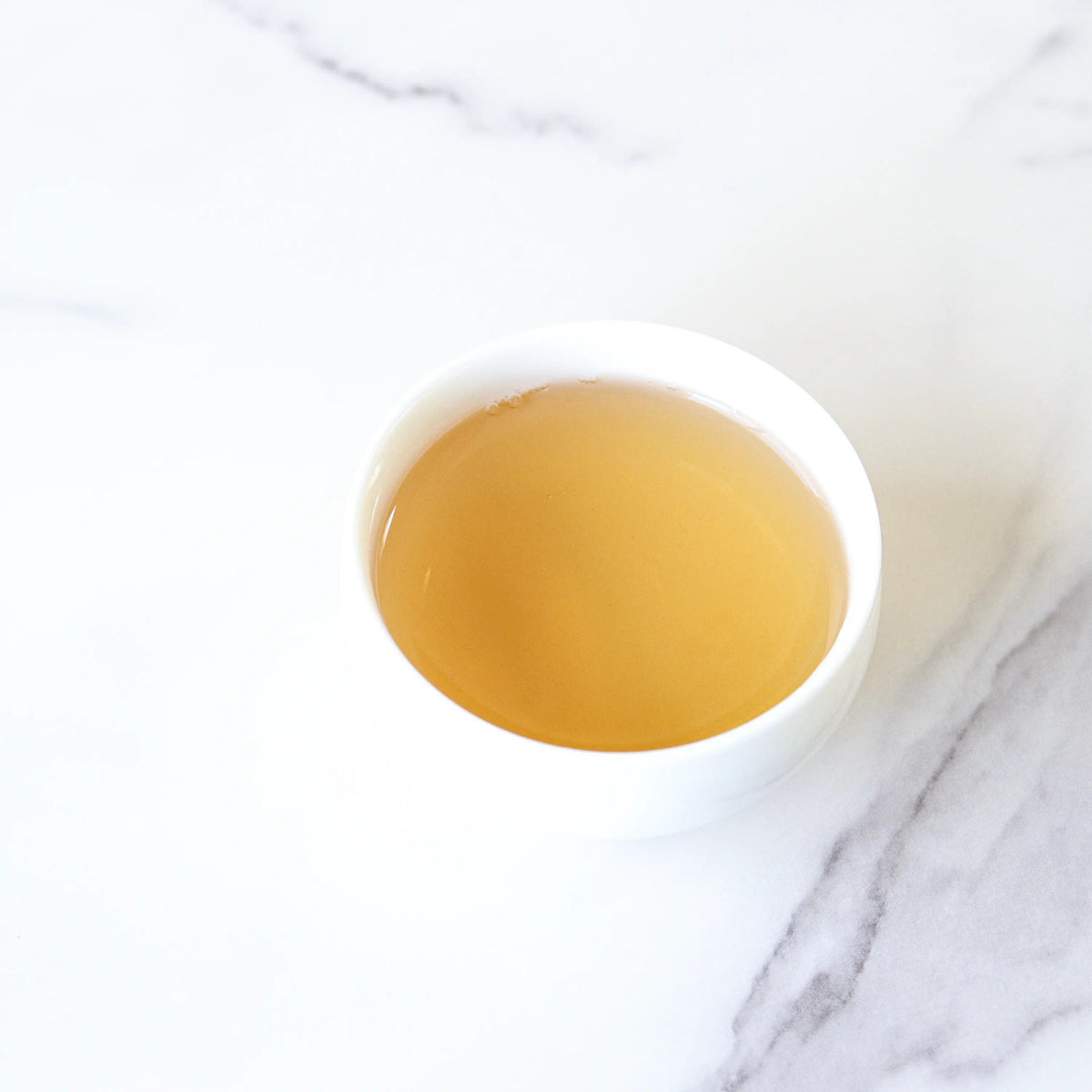 Brewed Phoenix Dancong oolong tea in a small white bowl on a white marble surface.