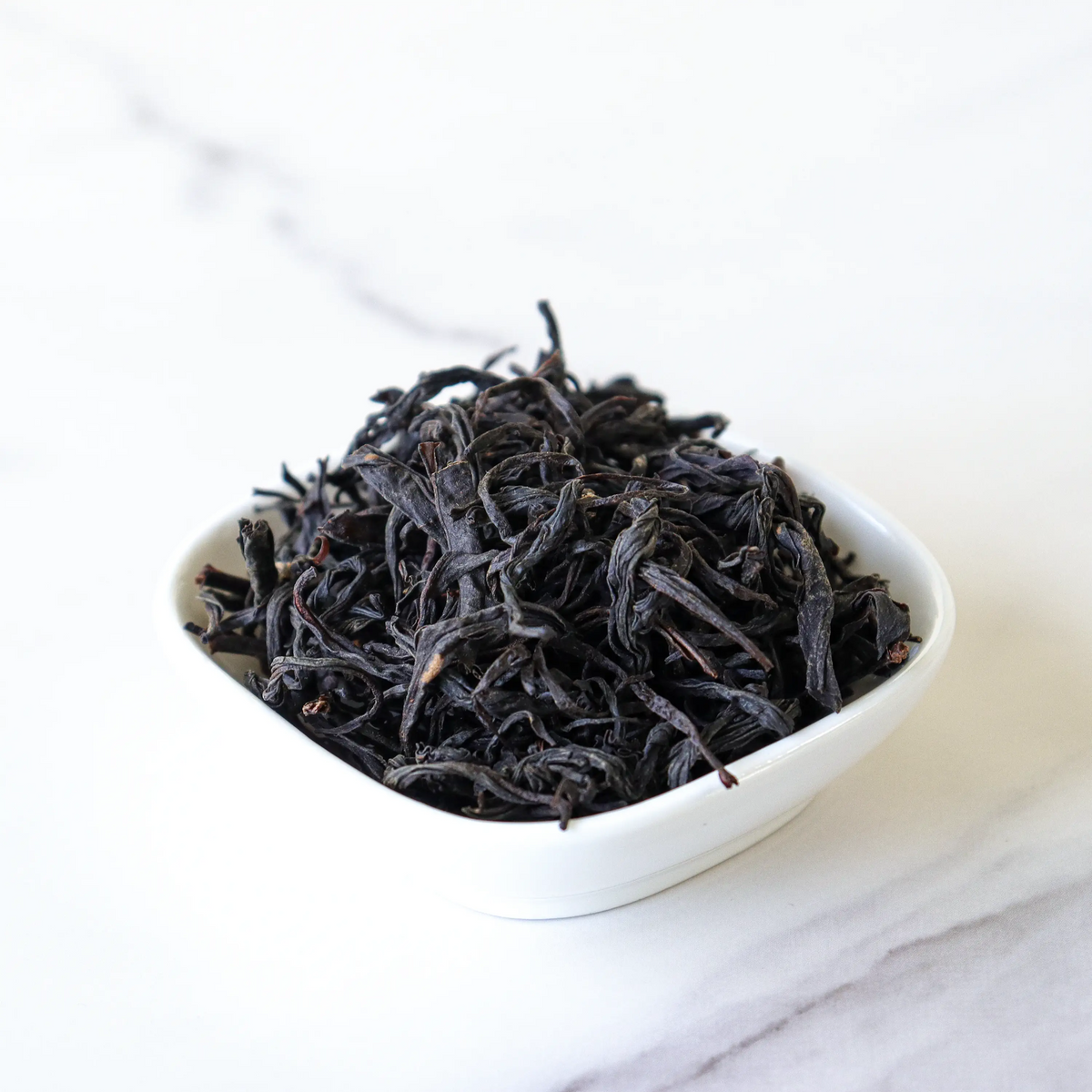Loose dried Phoenix Dancong oolong leaves in a small white bowl on marble.