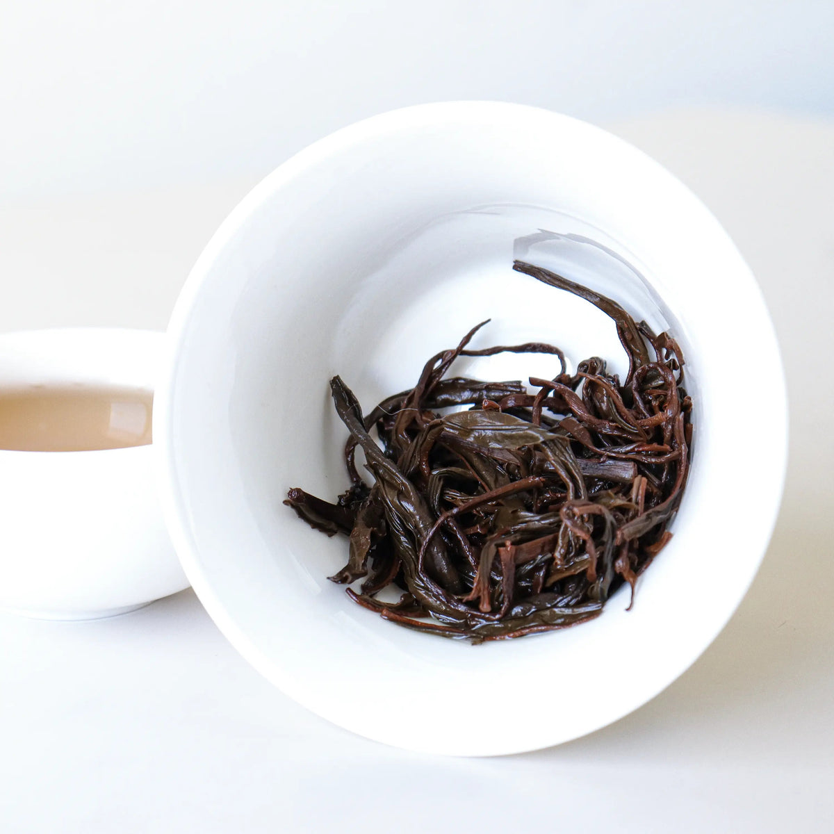 Steeped Phoenix Dancong oolong leaves in a tilted white bowl beside brewed tea.