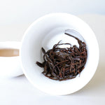 A white bowl of steeped Phoenix Dancong Oolong Tea from My Store is tilted to reveal the leaves, with a cup of the floral tea beside it.