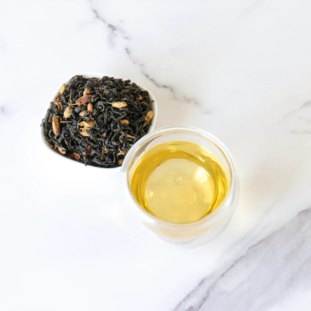 Pomelo Flower Green Tea leaves beside yellow tea liquor in a glass cup