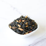 A small white bowl filled with Pomelo Flower Green Tea by My Store, a blend of loose leaf green tea and dried spices, rests on a white marble surface—ideal for anyone seeking a soothing wellness tea experience.