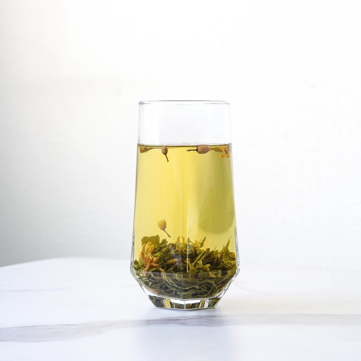 Pomelo Flower Green Tea brewed in a clear glass with leaves and buds at the bottom