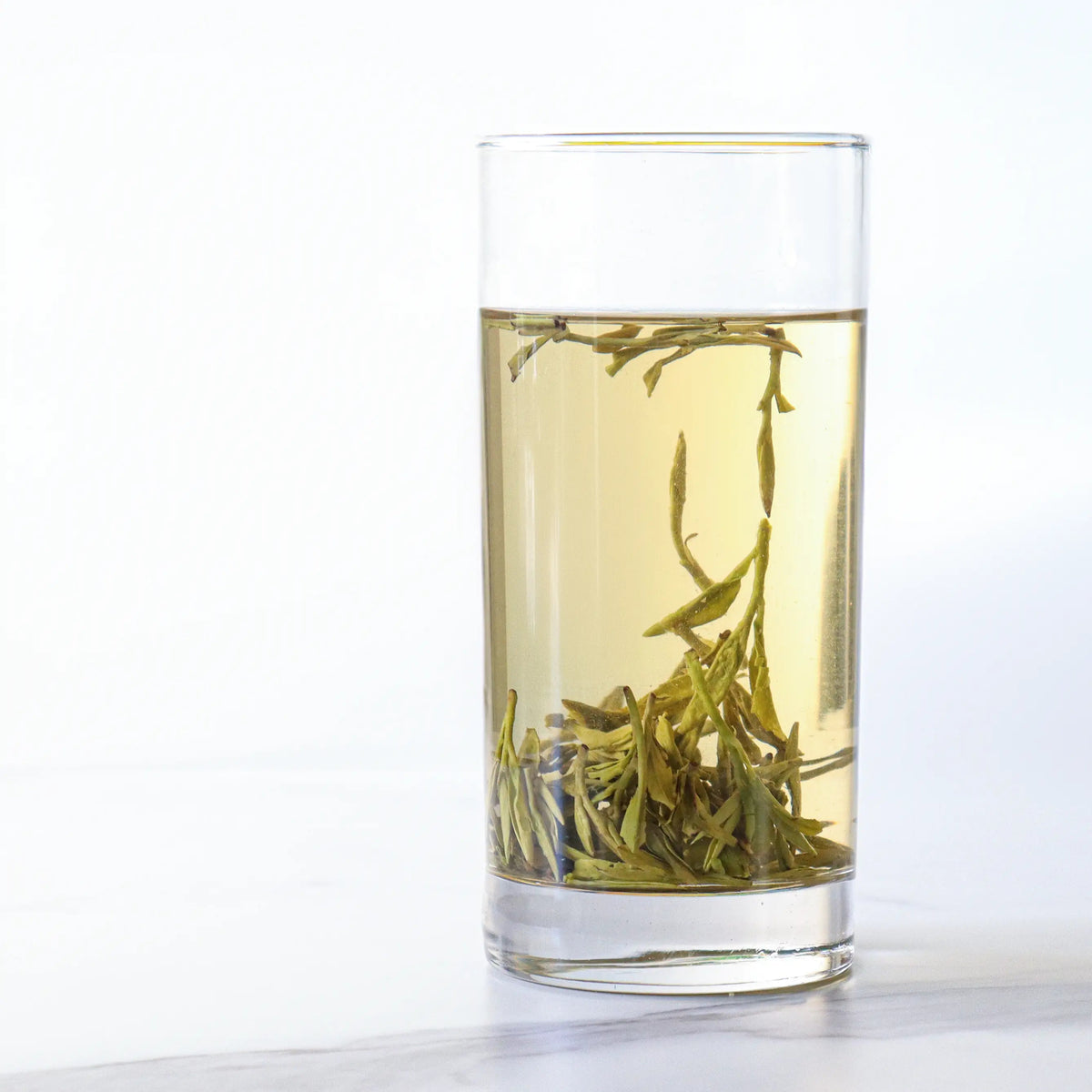 Premium West Lake Longjing Tea brewed in a tall glass with pale golden liquor and leaves.